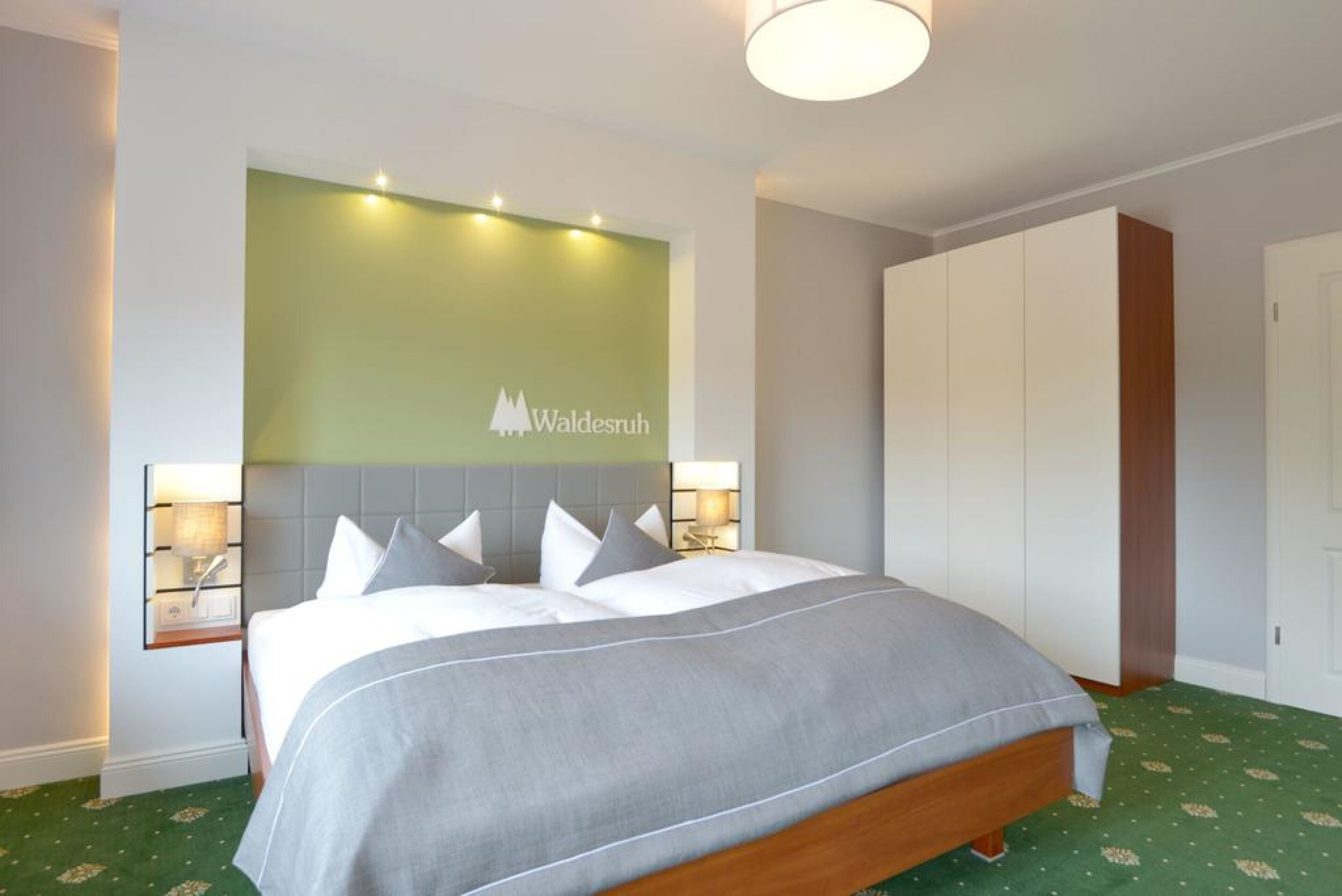 Una habitación de hotel con una cama, mesitas de noche, una pared verde y un armario.
