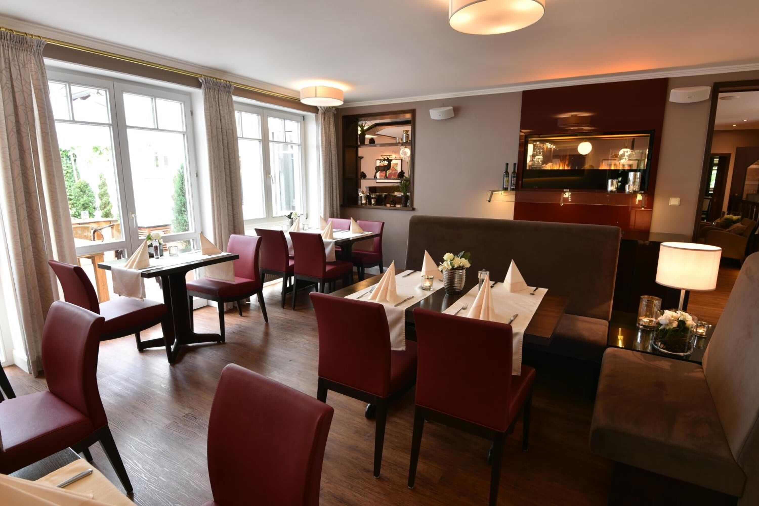 Un comedor con sillas y mesas rojas, un sofá y una zona de bar con televisor.