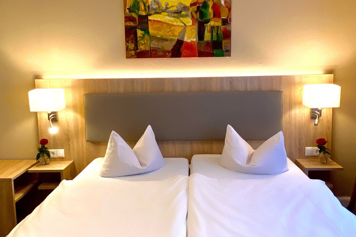 A hotel room with a double bed, two bedside tables with lamps, and a painting above the bed.