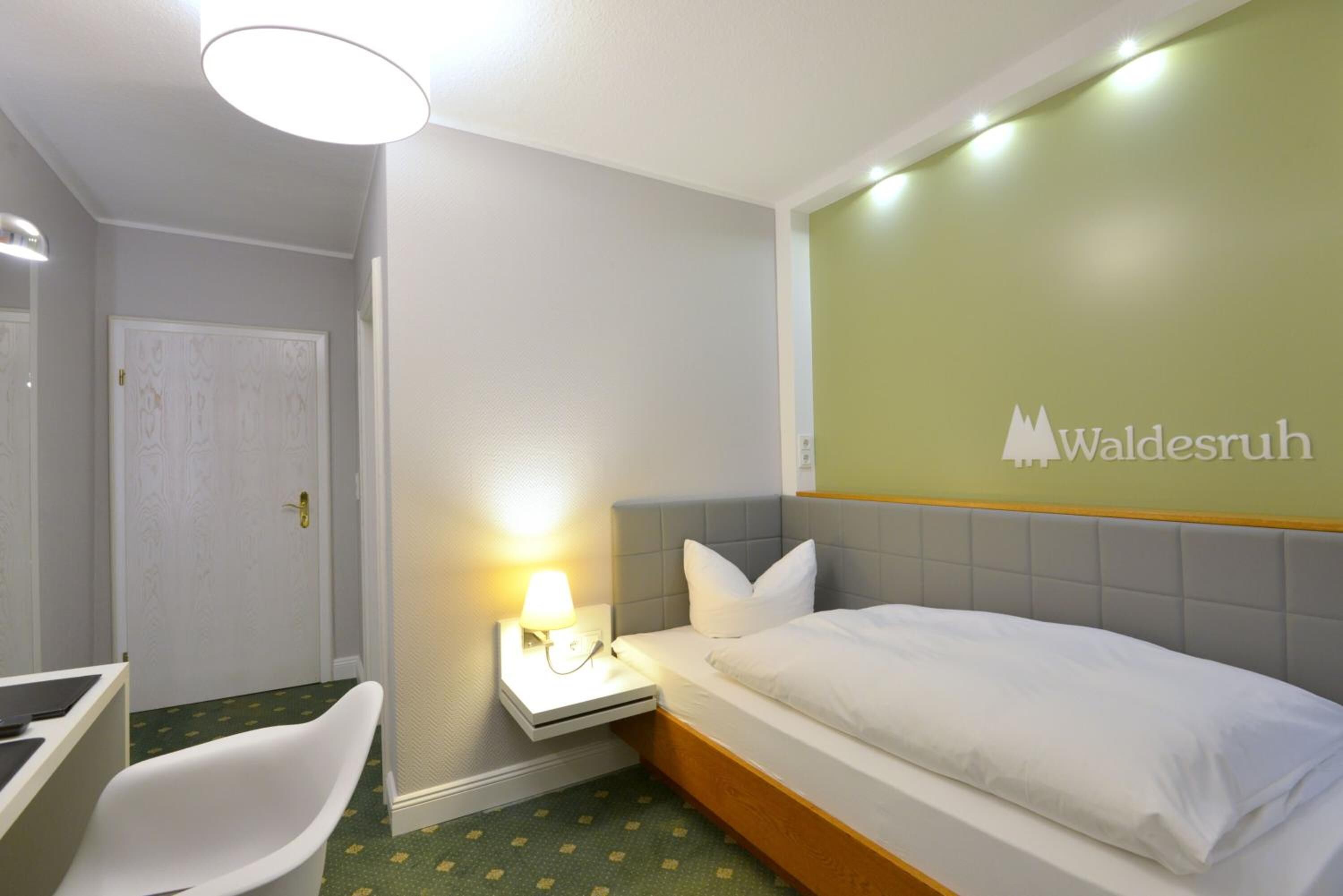 Una habitación de hotel con cama, escritorio, silla, mesita de noche con lámpara y puerta.