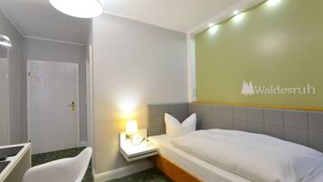 Una habitación de hotel con cama, escritorio, silla, mesita de noche con lámpara y puerta.