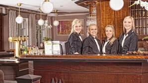 A reception desk with a logo, three staff members, and a bar area with bottles and glasses. - Hotel Restaurant Waldesruh (Emstek)