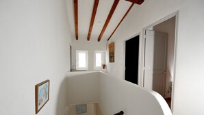 Una escalera con vigas de madera, paredes blancas y dos ventanas.
