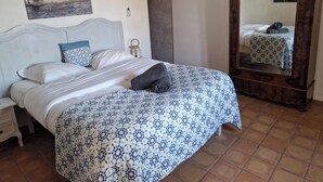 Una cama bien hecha con una colcha estampada, una mesita de noche con una lámpara y un espejo en la pared.