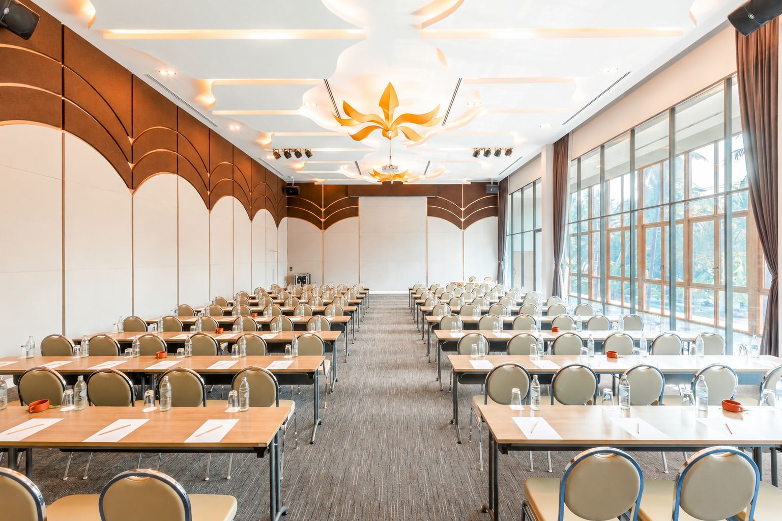 A conference room with rows of tables and chairs, large windows, and a modern ceiling design.