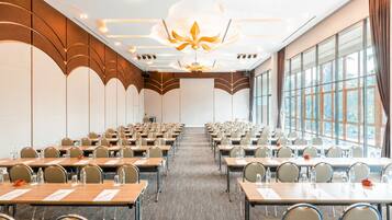 A conference room with rows of tables and chairs, large windows, and a modern ceiling design.