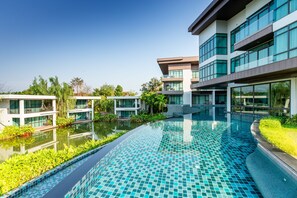 A modern hotel with a swimming pool, large windows, and a landscaped garden. - Na Tree Tara Riverside Resort Amphawa Damnoensaduak (Bang Khonthi)