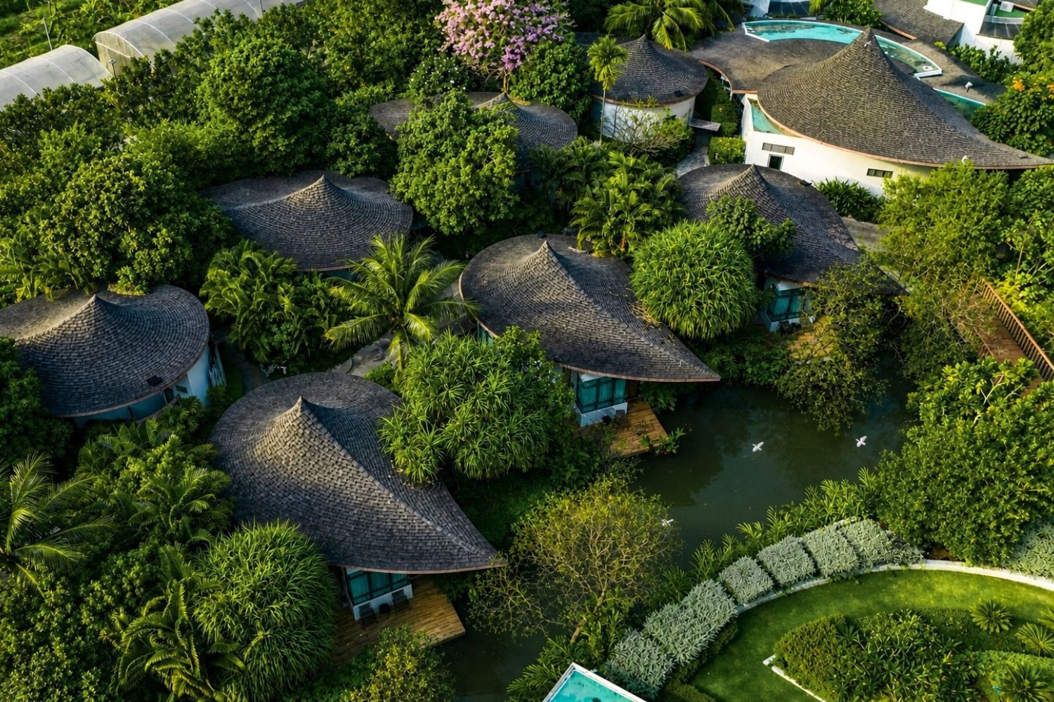 A resort with multiple bungalow-style buildings surrounded by lush greenery and a central water body.
