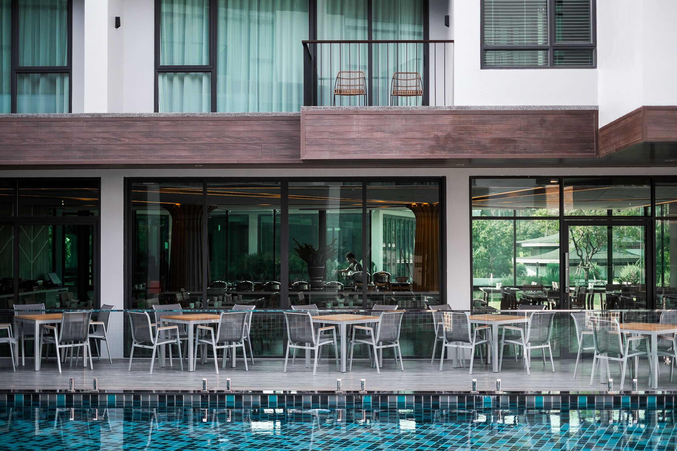 Un espacio exterior moderno para comer con mesas y sillas, una piscina y vistas al verdor.