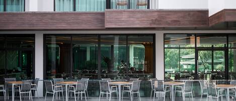 Un espacio exterior moderno para comer con mesas y sillas, una piscina y vistas al verdor.