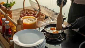 A breakfast setup with eggs being fried, condiments, and a basket of eggs on a table.