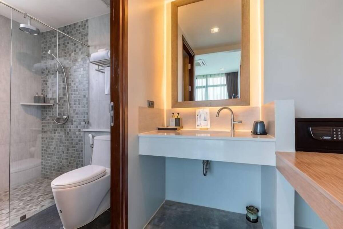 A modern bathroom with a glass shower enclosure, a white toilet, a sink with a mirror, and a microwave.