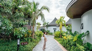 A pathway lined with lush greenery and palm trees, leading to a building with a curved roof and a sign indicating 'A05'. - Na Tree Tara Riverside Resort Amphawa Damnoensaduak (Bang Khonthi)