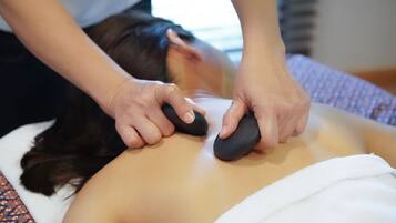 A massage therapy session with a person lying face down on a massage table, receiving pressure on the back with two massage tools.