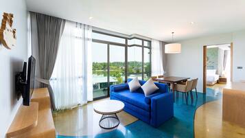 Una habitación de hotel moderna con un ventanal grande, un sofá azul, una mesa de centro redonda y un comedor.