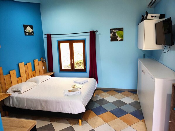 Una habitación con una cama, una ventana con cortinas, una mesita y un televisor sobre un mueble.