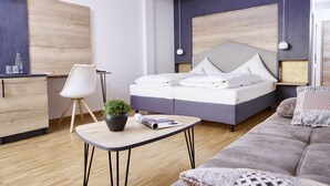 Un dormitorio moderno con cama, una mesita con una planta, un sofá y un escritorio con silla.