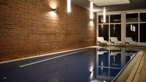 Una piscina interior con pared de ladrillo y sillas de descanso blancas.