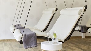 Una habitación con dos sillones reclinables, una mesita redonda con una botella y vasos, y una manta gris sobre uno de los sillones.