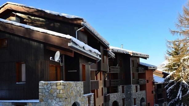 Un edificio cubierto de nieve con muros de piedra y balcones de madera, probablemente un hotel o una posada en una zona montañosa.