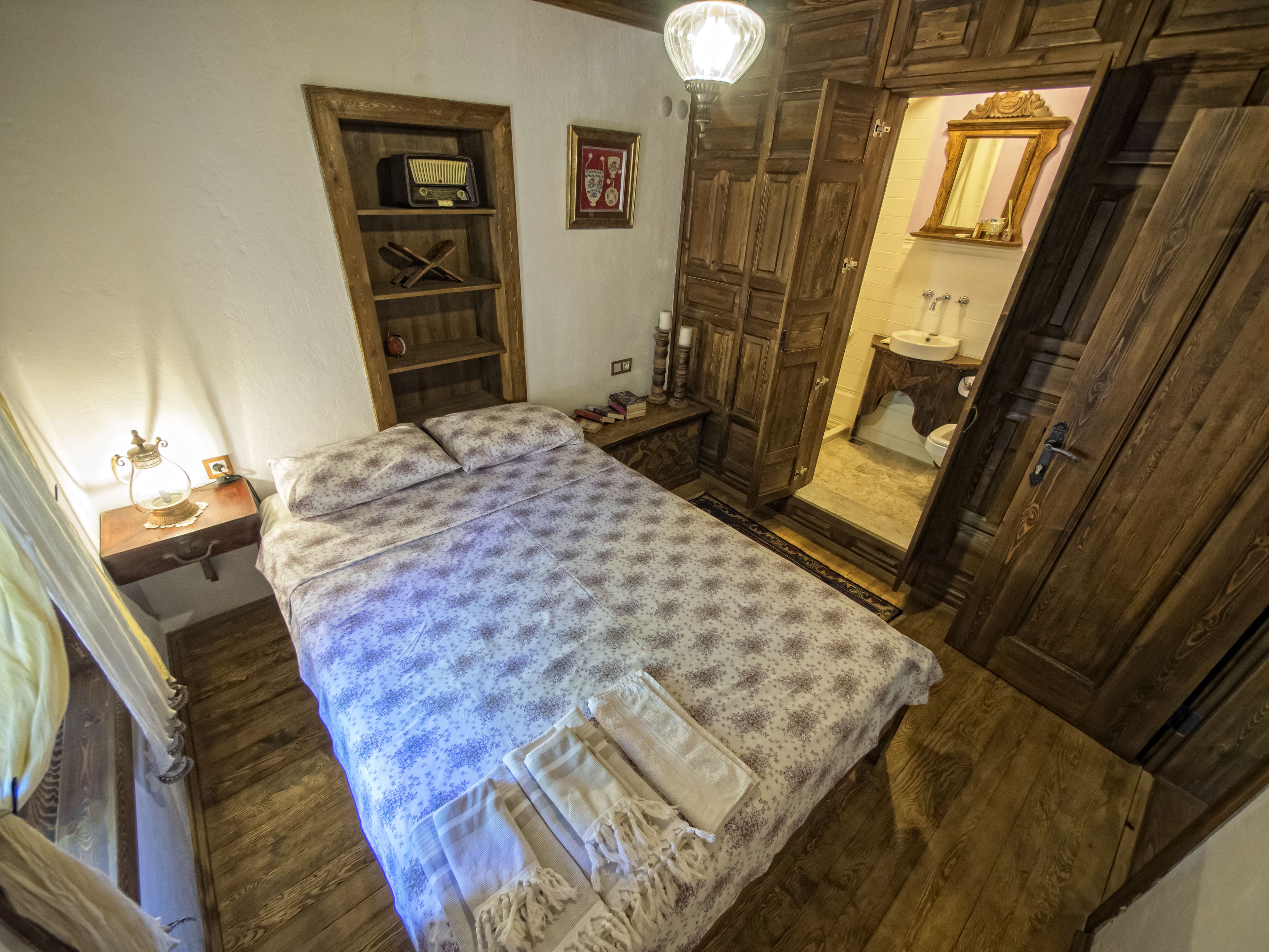 A bedroom with a bed, wooden wardrobe, and a small bedside table with a lamp.