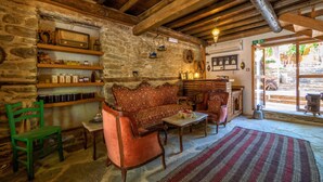 A rustic interior with stone walls, wooden beams, a patterned sofa, a green chair, and a rug. - Birgi Yeni Gelin Evi (Odemis)