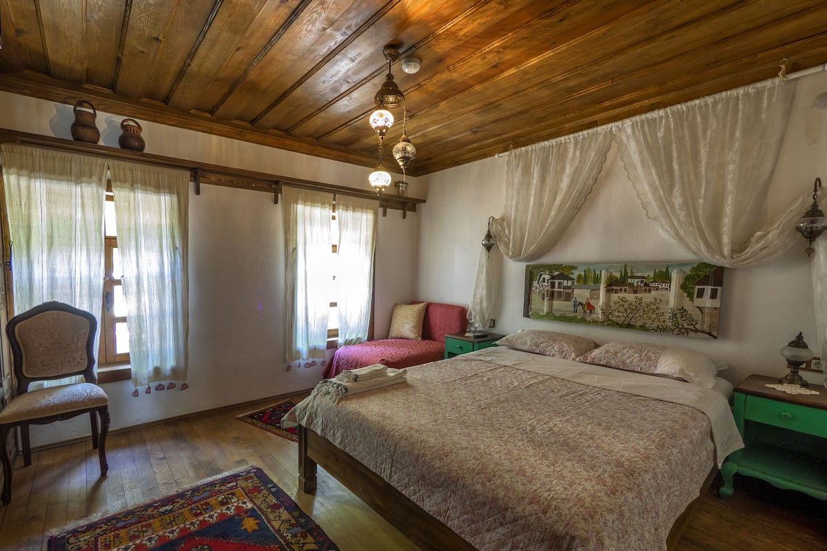 Una camera da letto tradizionale con soffitto in legno, un letto grande con biancheria da letto a fiori, una sedia, un comodino e un quadro appeso al muro.