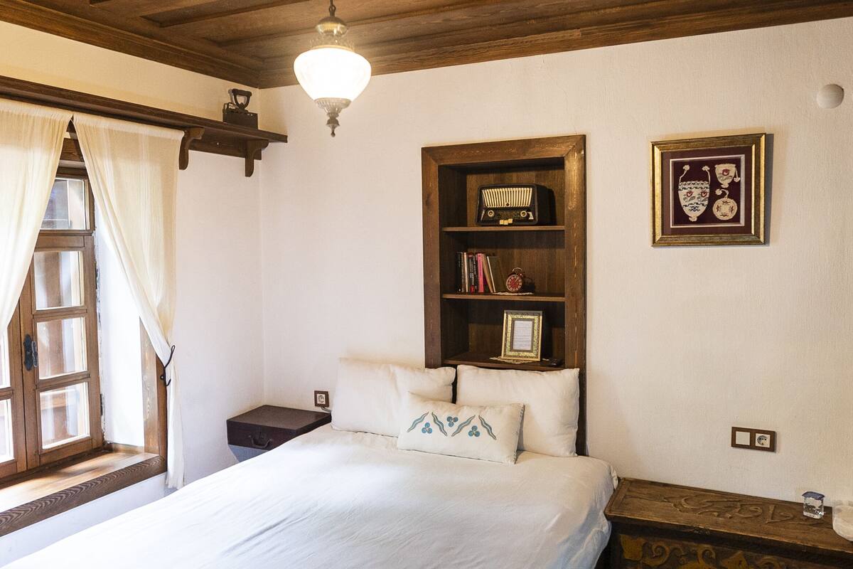 Una camera da letto con un letto, un comodino, una mensola e una finestra con tende.