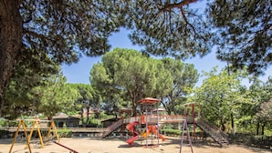A playground with swings, slides, and climbing structures surrounded by trees and stone pathways. - Birgi Yeni Gelin Evi (Odemis)