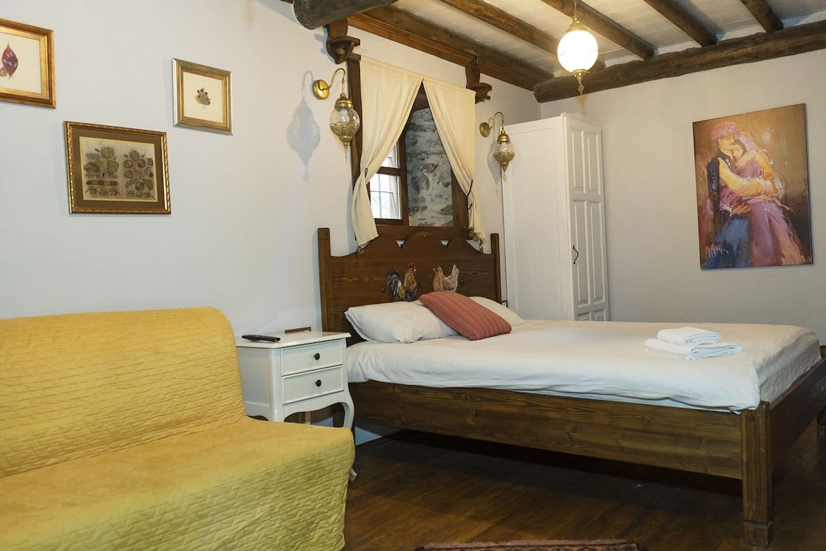 Una camera da letto con un letto di legno, un comodino, una poltrona gialla e un quadro appeso al muro.