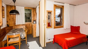 A compact room with a wooden table, a single bed with a red cover, a window with a view, and a ceiling lamp. - Divisible studio for 3, near shops and slopes, free parking, balcony (Bellentre)