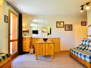 A compact room with a wooden dining table, a sofa, and a small kitchen area with a mirror and a sink.