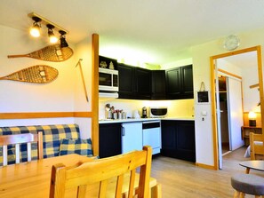 A compact kitchen with dark cabinets, a microwave, and a coffee maker. There's a wooden dining table with chairs and a checkered bench.