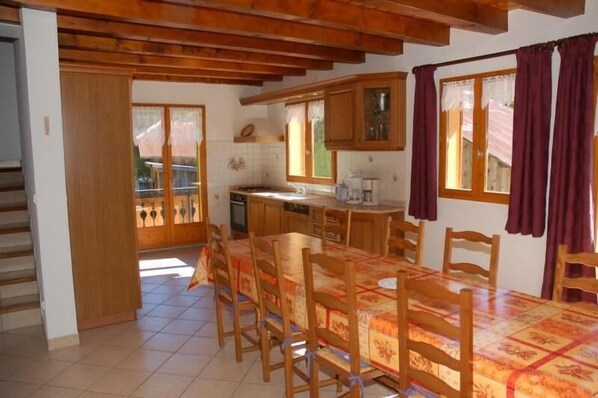 A kitchen with wooden cabinets, a dining table with chairs, and a window with curtains. - chalet la grange du villard le criou (Samoëns)