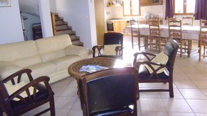 Ein Wohnzimmer mit einer Couch, Sesseln, einem Couchtisch und einer Treppe, die in einen Küchenbereich mit Esstisch und Stühlen führt.