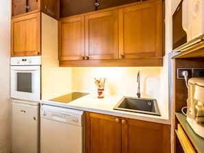 A compact kitchen with wooden cabinets, a white oven, a dishwasher, and a sink with a faucet.