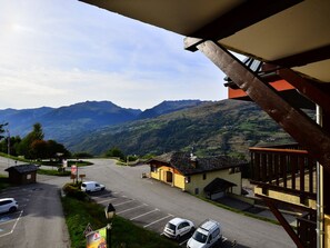 A parking lot with several cars, a small building with a sloped roof, and a mountain range in the background.