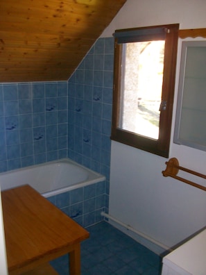 Ein kleines Badezimmer mit Holzboden, einer Badewanne und blauen Fliesen.