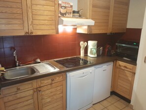 Eine kompakte Küche mit Holzausstattung, einem integrierten Geschirrspüler, einem Kochfeld und einer Kaffeemaschine.