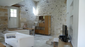 Una sala de estar moderna con pared de piedra, un sofá blanco, un mueble de madera y una televisión.