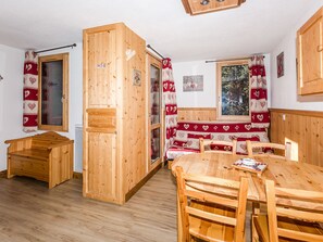 Interior de una cabaña de madera con una mesa de comedor, sillas, un banco y un ventanal con vistas a árboles.