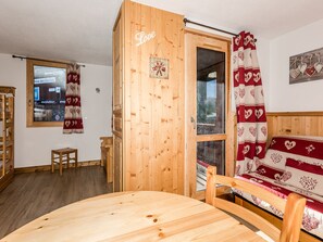 Una habitación acogedora con una puerta de madera, una cama con ropa de cama estampada con motivos de corazones, una pequeña mesa de madera y una ventana con vistas al exterior.