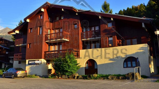 Un immeuble à plusieurs étages doté de balcons, d’un panneau indiquant un chalet de ski et d’un espace de stationnement.