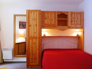 Ein Schlafzimmer mit einem Holfischschrank, einem Bett mit roter Decke und zwei Nachttischlampen.