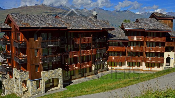 A chalet-style building with multiple balconies, stone foundations, and a mountainous backdrop. - 2-Room Apartment with Balcony, Ski Access, and Free Parking - Montchavin Les Coches (Bellentre)