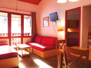 Ein gemütliches Zimmer mit einem roten Sofa, einem Holztisch und einem an der Wand befestigten Fernseher.