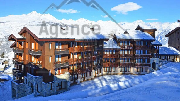 Eine schneebedeckte Lodge mit mehreren Balkonen und einem Bergpanorama im Hintergrund.