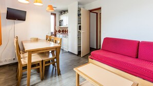 Ein kompakter Wohnraum mit Essbereich, einer Küchenzeile und einem roten Sofa.