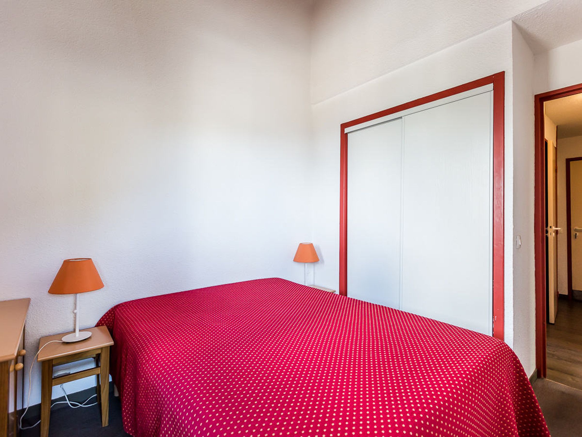Ein Schlafzimmer mit einem Bett, zwei Nachttischlampen, einem Kleiderschrank und einem Schreibtisch mit Lampe.
