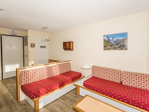 A room with two red patterned sofas, a wooden table, a lamp, a picture on the wall, and a door with a notice.